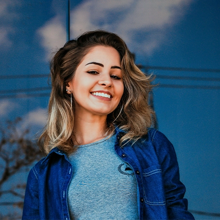 Lady with a nice smile wearing a denim jacket and standing in front of a reflective window