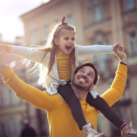 Man and child wearing matching yellow sweaters as the girl rides on his shoulders